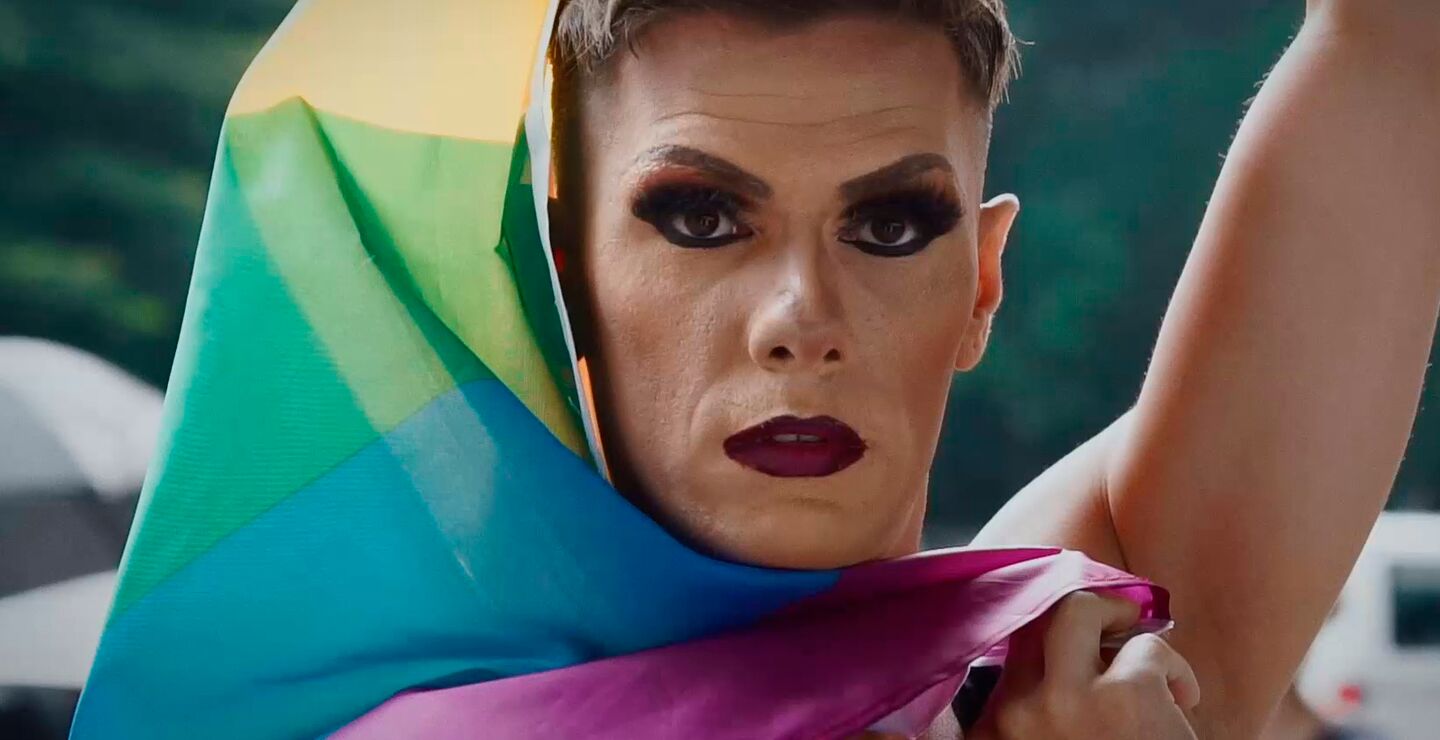 A man with makeup holding a pride flag