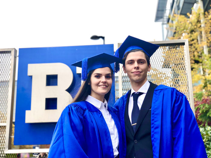  Two people who are graduating standing in front of the BI sign